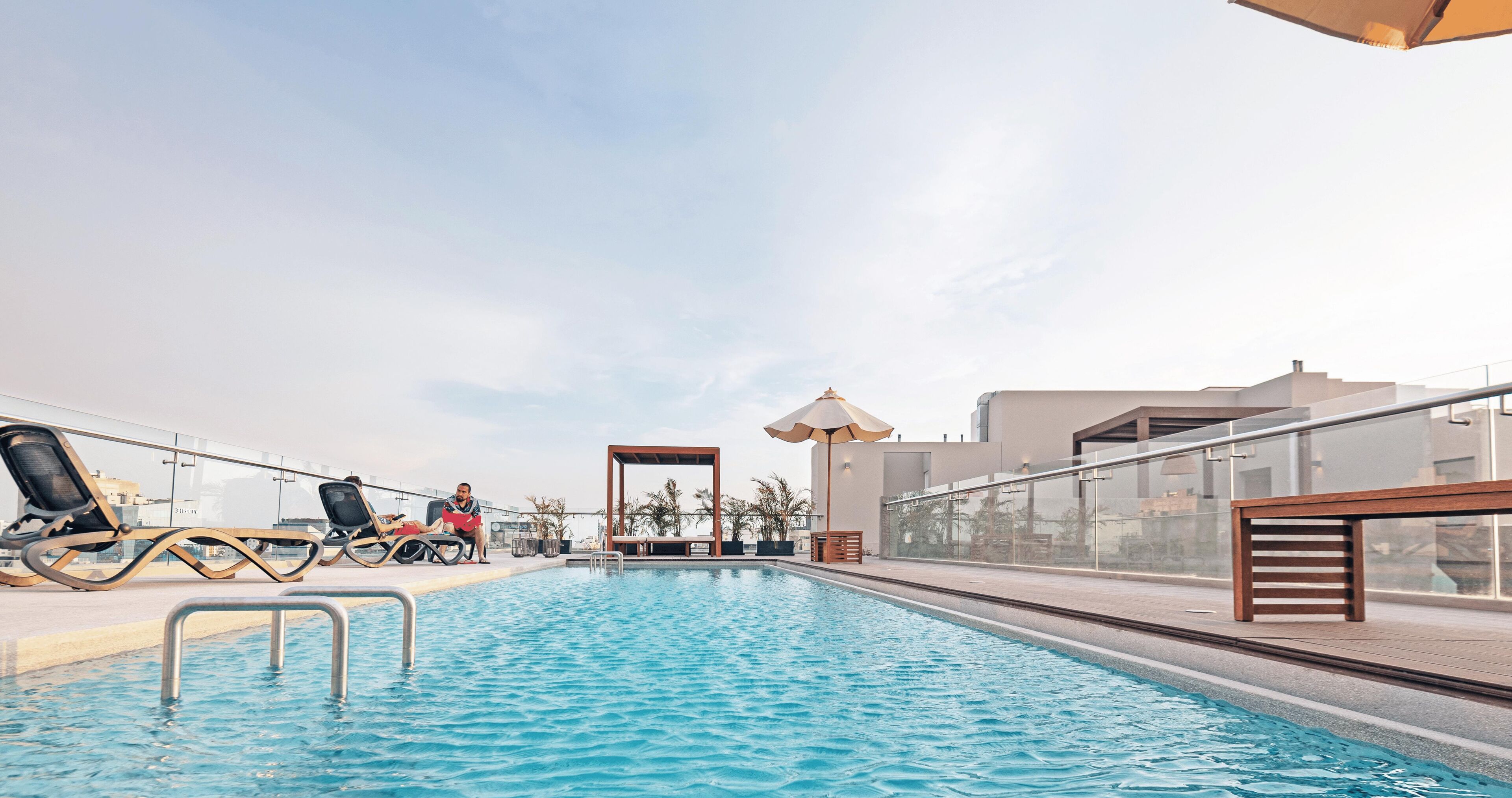 A rooftop pool with lounge chairs and umbrellas, surrounded by modern buildings.