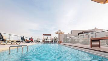 A rooftop pool with lounge chairs and umbrellas, surrounded by modern buildings.