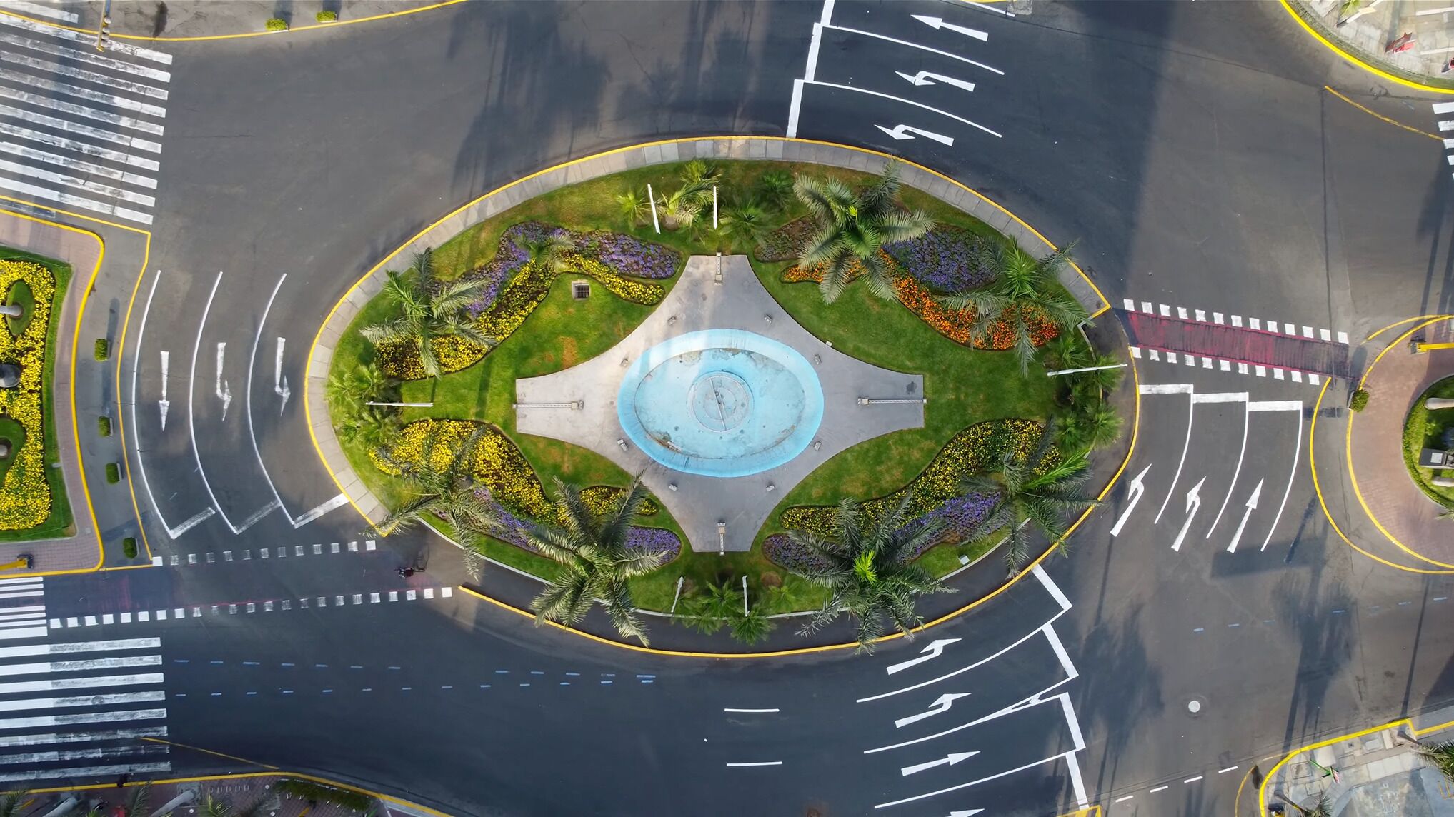 A roundabout with a central fountain, surrounded by landscaped areas with various plants and flowers.
