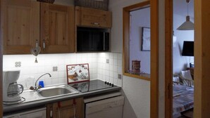 A compact kitchen with wooden cabinets, a built-in microwave, and a small sink. - 100m from ski slopes, 3rd floor, view ski slopes, balcony, tv, ski locker, 32m², La Plagne (La Plagne)
