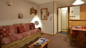 A cozy living room with a wooden sofa, a dining table with a red tablecloth, and a mirror on the wall. - 100m from ski slopes, 3rd floor, view ski slopes, balcony, tv, ski locker, 32m², La Plagne (La Plagne)