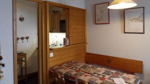 A compact room with a wooden bed, a small table, and a mirror. - 100m from ski slopes, 3rd floor, view ski slopes, balcony, tv, ski locker, 32m², La Plagne (La Plagne)