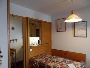 A compact room with a wooden bed, a small table, and a mirror. - 100m from ski slopes, 3rd floor, view ski slopes, balcony, tv, ski locker, 32m², La Plagne (La Plagne)
