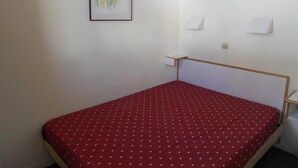 Una habitación pequeña con una cama individual, colcha roja, cabecero de madera y un cuadro en la pared.