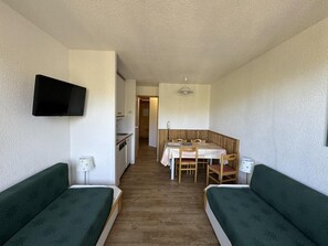 A compact room with two green sofas, a wooden dining table, and a TV mounted on the wall. - Ski-in/ski-out & foot of the slopes, 4th floor, view ski slopes, balcony, tv, ski locker, 24m² (La Plagne)