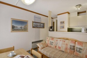 Ein gemütliches Zimmer mit einer Couch, einem Esstisch mit Tasse und Untertasse sowie gerahmten Bildern an der Wand.