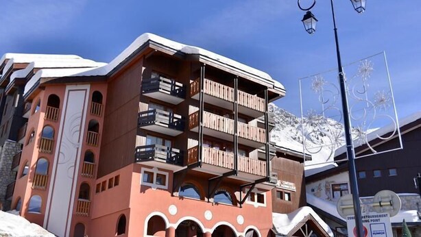 Un hôtel à plusieurs étages doté de balcons, avec une piste de ski en arrière-plan et un panneau indiquant un point d’intérêt touristique.