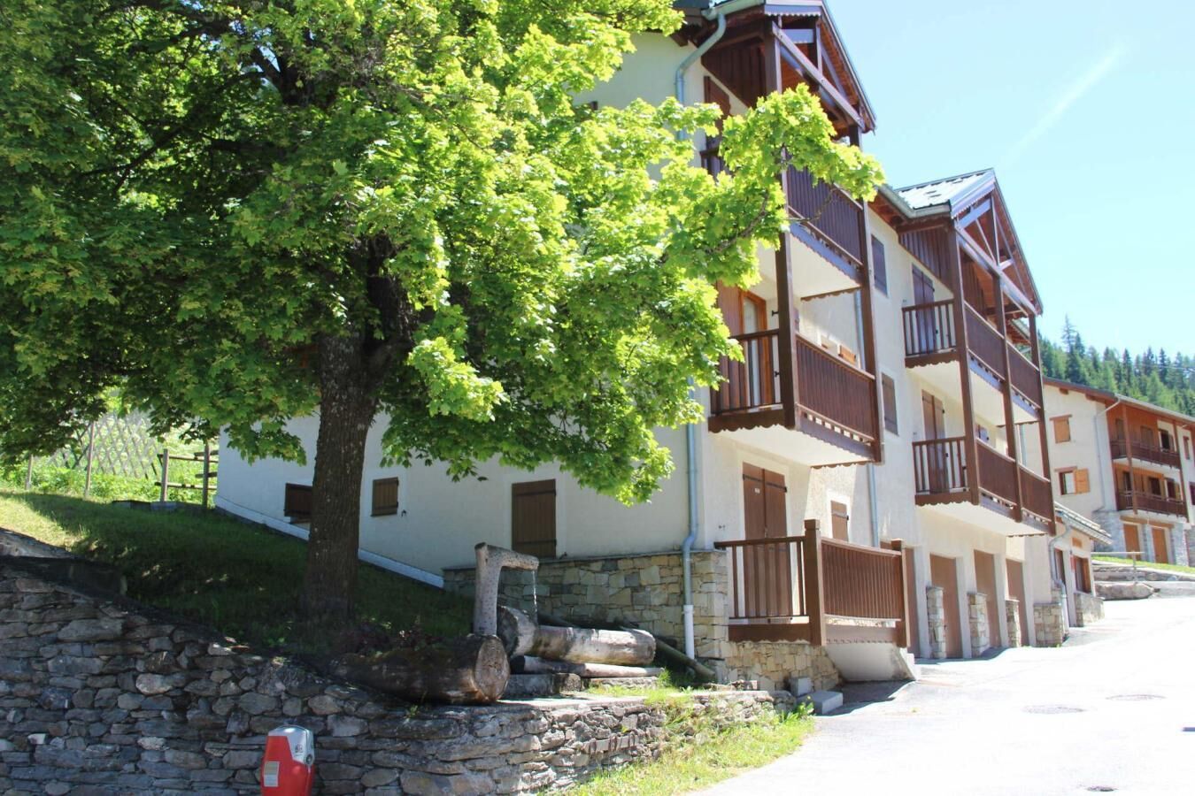 A row of traditional chalet-style buildings with balconies, stone foundations, and a stone wall in the foreground.