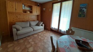 A room with a sofa, a dining table with chairs, a wooden cabinet, and a window with curtains. - 350m from ski slopes, balcony, parking, tv, ski locker, 24m², Valloire (Valloire)