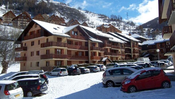 A multi-story hotel with balconies, a parking lot with cars, and snow-covered mountains in the background. - 350m from ski slopes, balcony, parking, tv, ski locker, 24m², Valloire (Valloire)