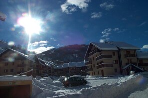 A snow-covered building with multiple balconies, a parked car, and a mountain in the background. - 230m from resort center, balcony, parking, tv, ski locker, 24m², Valloire (Valloire)