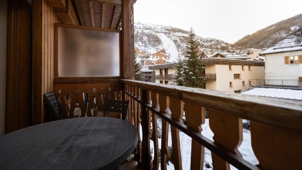 A wooden balcony with a table and chairs, overlooking a snowy mountain and buildings. - 300m from ski slopes, 2nd floor, balcony, ski locker, 38m², Valloire (Valloire)