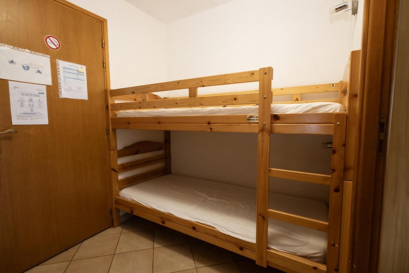 Un lit superposé dans une pièce avec une porte en bois et un sol carrelé.