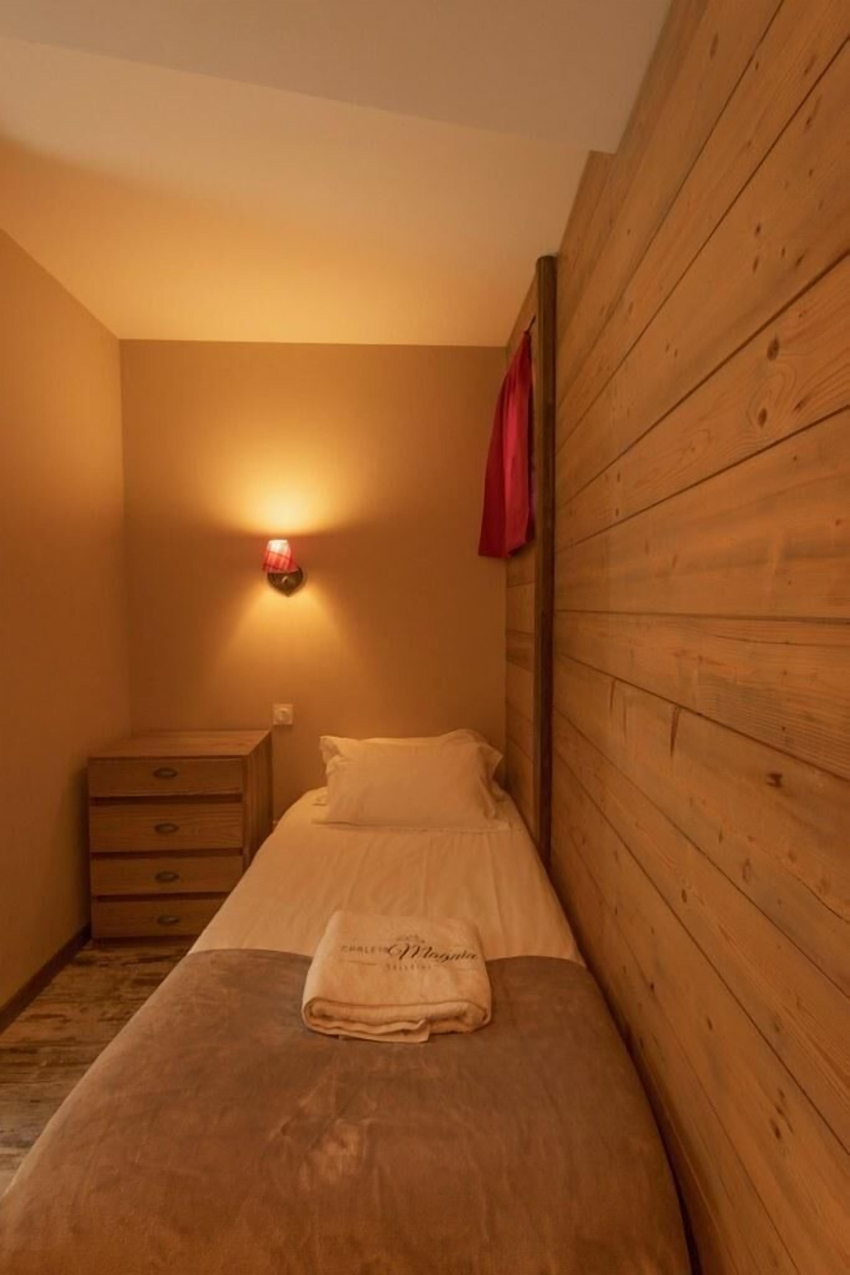 A small, cozy room with a single bed, a nightstand, and a wall-mounted light.