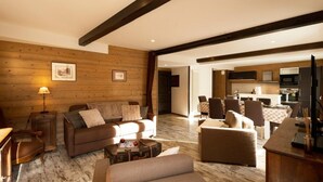 A cozy living room with a sofa, armchairs, and a coffee table. There is a wooden wall with framed pictures and a lamp. A kitchen is visible in the background. - 260m from ski slopes, 1st floor, terrace, balcony, tv, ski locker, 90m², Valloire (Valloire)