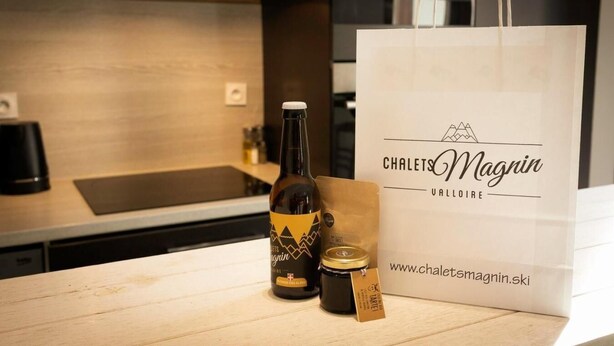 A bottle of Magrin wine, a jar of Magrin honey, and a white paper bag with the logo "Chalets Magrin Valloire" on a wooden table in a modern kitchen. - 260m from ski slopes, 1st floor, terrace, balcony, tv, ski locker, 90m², Valloire (Valloire)