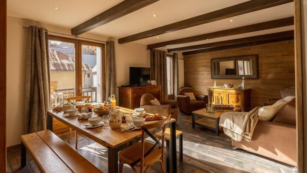 Un salon chaleureux avec une table à manger en bois, mise pour le petit-déjeuner, un canapé en cuir et un téléviseur posé sur un meuble en bois.