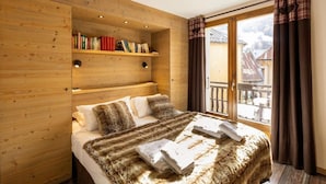 Une chambre chaleureuse avec une tête de lit en bois, une bibliothèque, un lit recouvert d’un plaid en fourrure et une vue sur les bâtiments par la fenêtre.