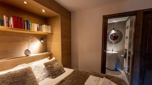 Une chambre à coucher avec une tête de lit en bois, une bibliothèque, un lit recouvert de coussins moelleux et une salle de bain visible à travers une porte ouverte.