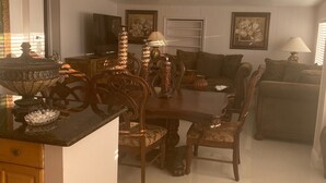 Ein Essbereich mit Holztisch und Stühlen, eine Küchenzeile und ein Wohnzimmer mit Sofa und Fernseher.