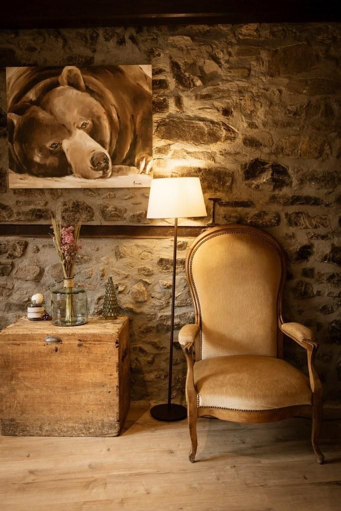 A rustic room with a stone wall, a wooden chest, a lamp, and a chair.
