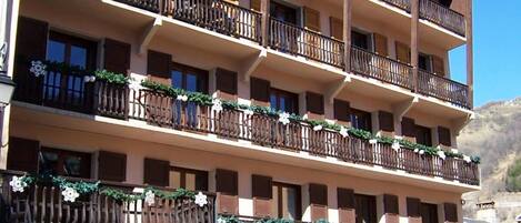 A multi-story hotel with wooden balconies, stone facade, and a storefront with signage.