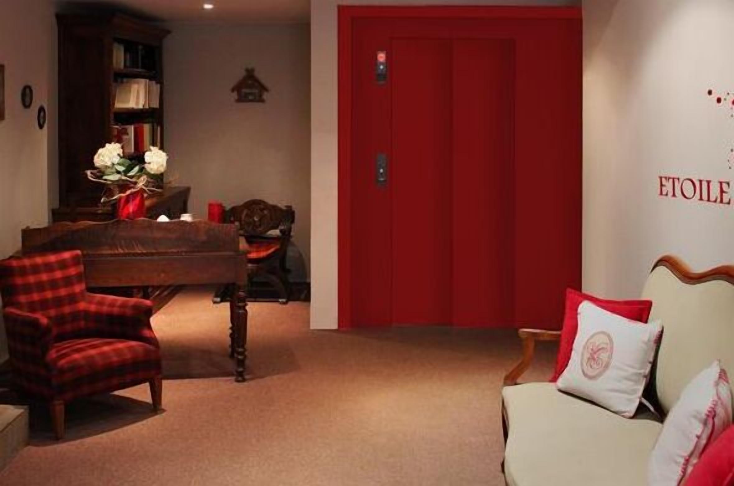 Ein Zimmer mit roter Tür, einem Klavier, einem rot-schwarz karierten Sessel und einem beigen Sofa mit roten Kissen.
