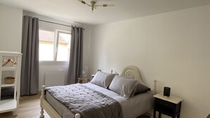 A bedroom with a bed, a nightstand, a chair, a window with curtains, and a ceiling fan. - Isabelle's Country House (Germaine)