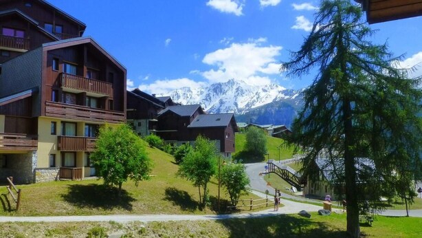 Ein Bergort mit Holzbauten, einer Seilbahn und schneebedeckten Gipfeln im Hintergrund.