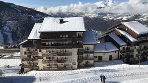 Ein schneebedecktes Gebäude mit mehreren Balkonen und einer Bergkulisse.