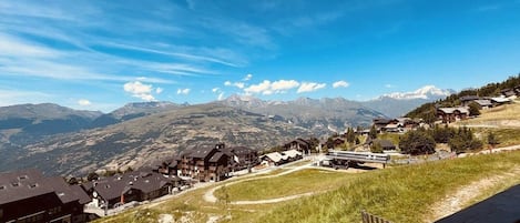 A mountain village with traditional houses, a clear sky, and a view of distant snow-capped mountains.