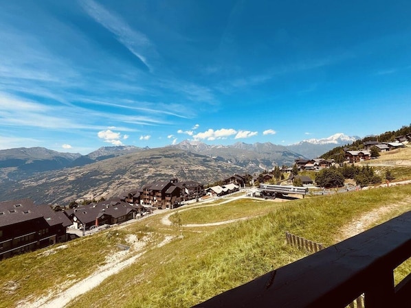 A mountain village with traditional houses, a clear sky, and a view of distant snow-capped mountains.