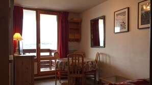 A cozy room with a dining table set for two, a wooden cabinet, and a bed with a red blanket.