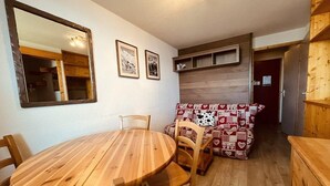 A cozy room with a wooden dining table and chairs, a sofa with a heart-patterned cover, and a wooden headboard.