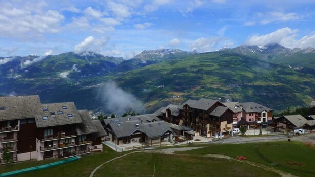 A mountain resort with chalet-style buildings, a ski lift, and a view of snow-capped mountains.