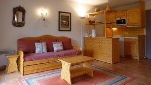 A cozy living room with a wooden sofa, a small wooden table, and a kitchen area with wooden cabinets and a microwave.