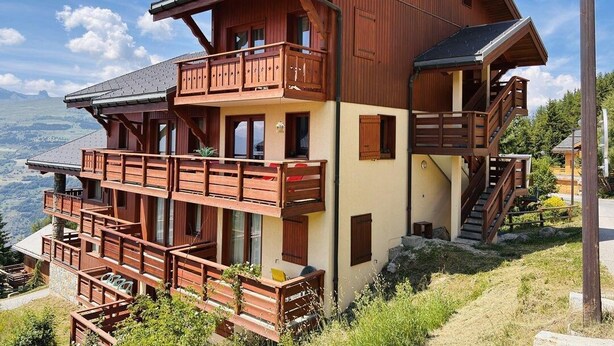A multi-story wooden chalet with balconies, a staircase, and a view of the landscape.
