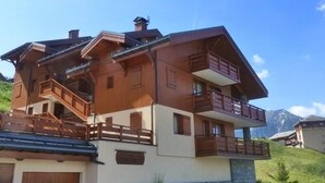 A multi-story wooden chalet with balconies, a garage, and a view of mountains.