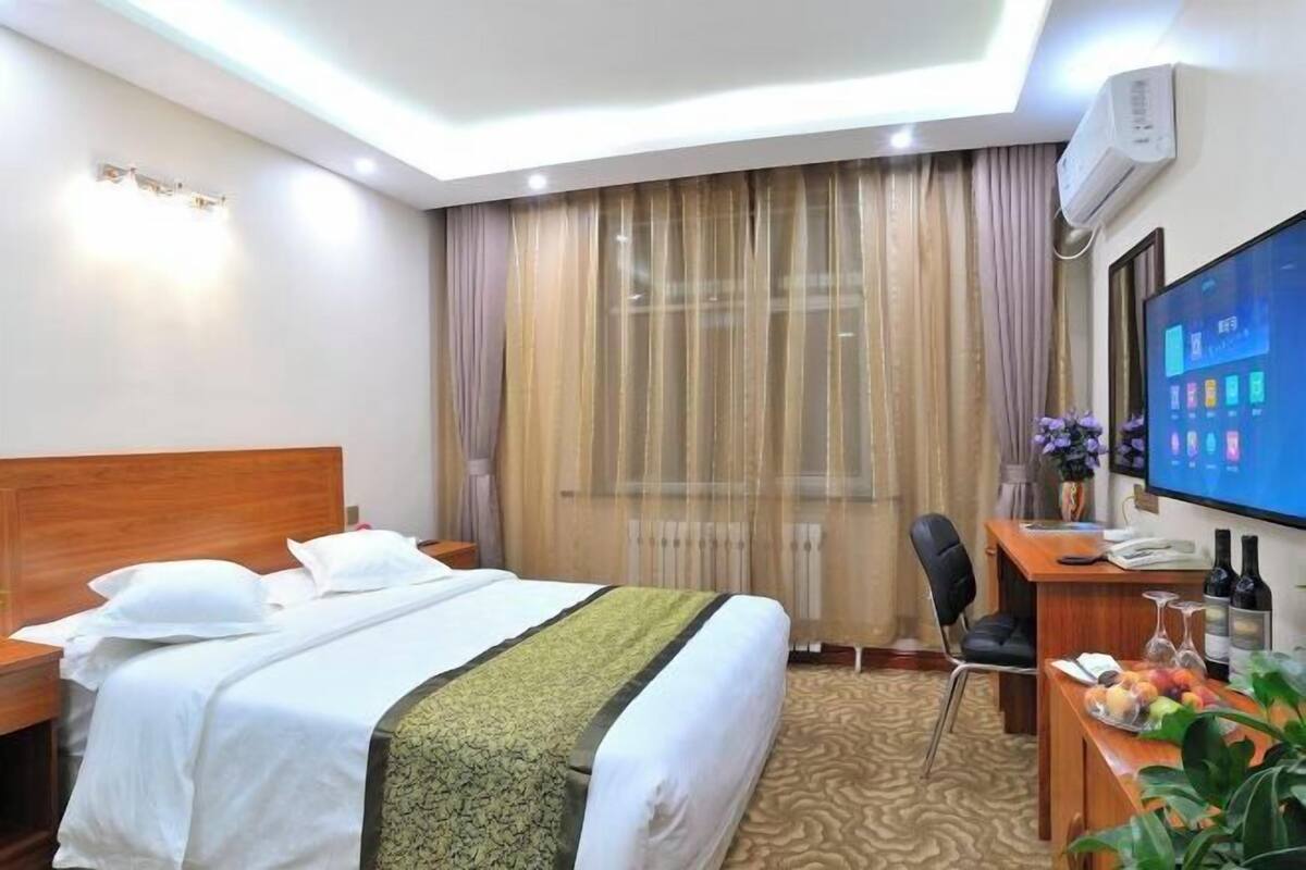 A hotel room with a bed, a desk with a computer, a television, and a window with curtains.