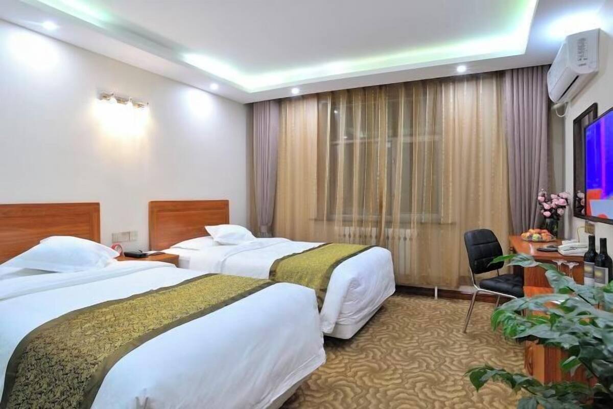A hotel room with two beds, a desk with a chair, a TV, and an air conditioning unit.