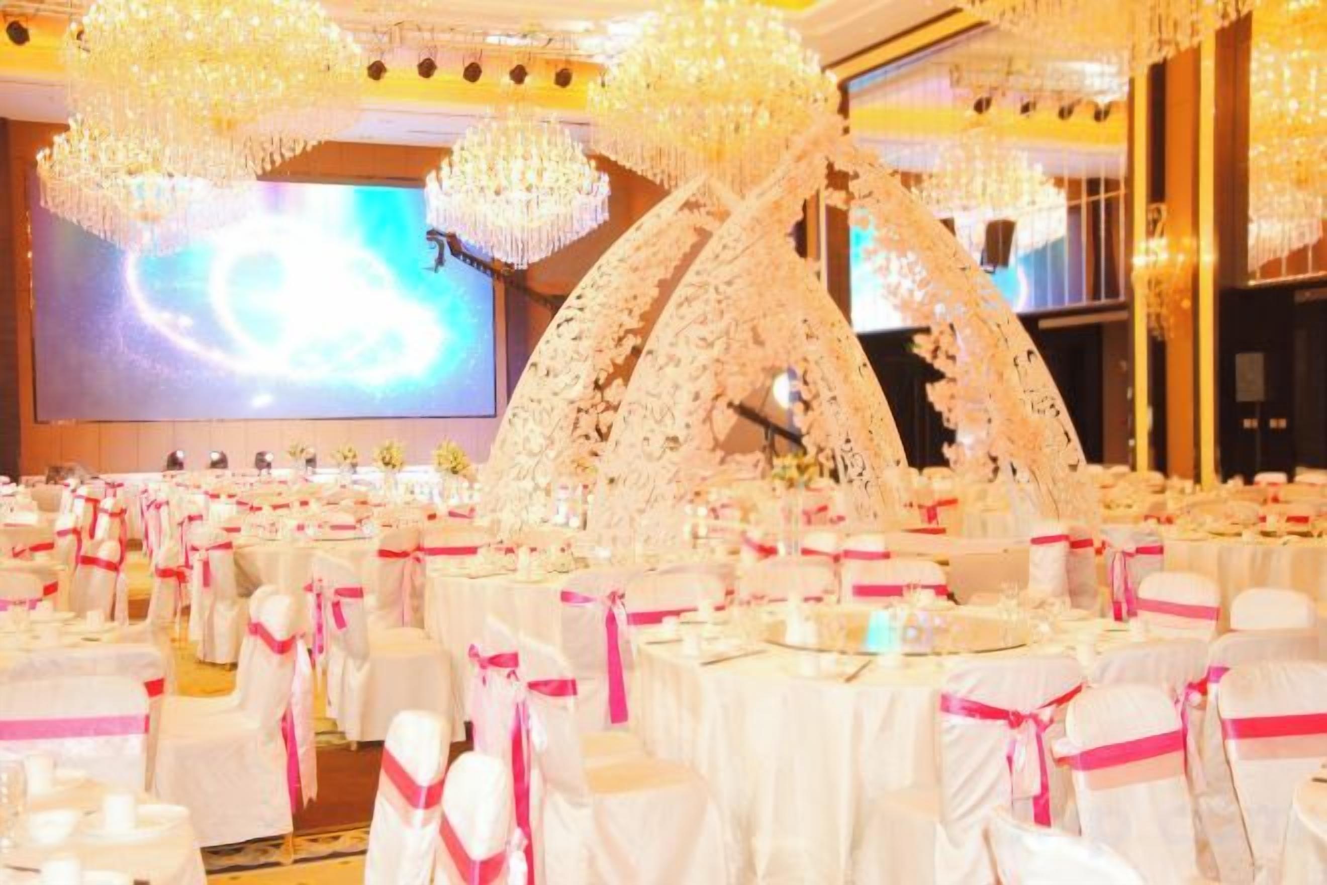 Una sala banchetti con tavoli rotondi, tovaglie bianche e nastri rosa.