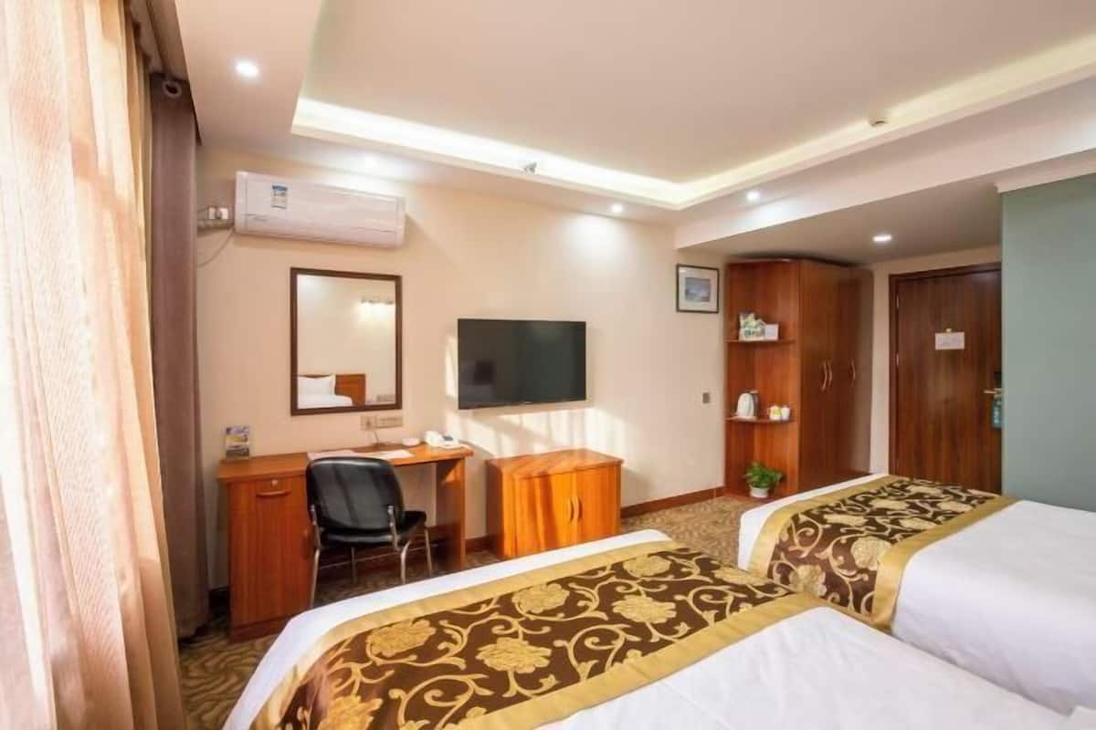 A hotel room with two beds, a desk, a chair, a television, and a wardrobe.