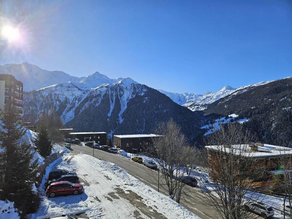 A snowy mountain landscape with a road, parked cars, and buildings.