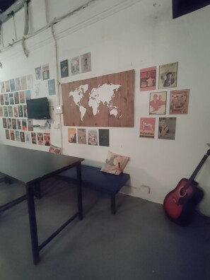 A room with a world map, posters, a TV, a guitar, and a table. - Backpacker Cowies (Mumbai)