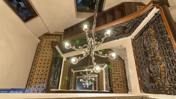 Un magnifique escalier orné de balustrades travaillées et surmonté d’un lustre.