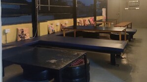 Une pièce avec des tables et des bancs, un ventilateur et un lustre.