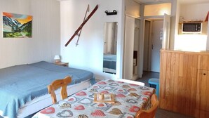 Een kleine kamer met een bed, een tafel met een tafelkleed met een patroon, een houten kast en een schilderij aan de muur.
