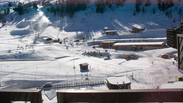 Estância de esqui coberta por neve, com teleféricos, edifícios e montanhas ao fundo.