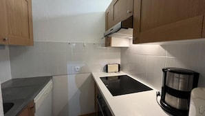 Cozinha compacta com armários de madeira, fogão por indução preto, torradeira e cafeteira.
