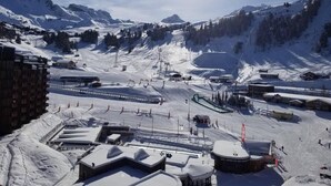 Uma estação de esqui com encostas cobertas de neve, um teleférico e edifícios em primeiro plano.